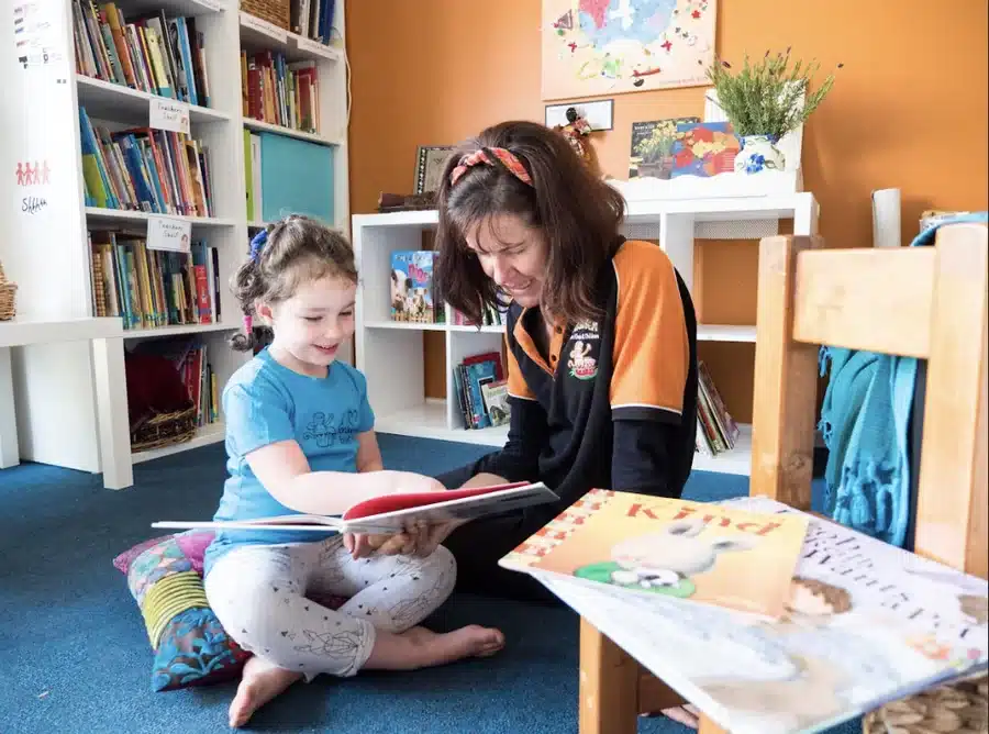 An educator reading a picture book with a child in the reading corner