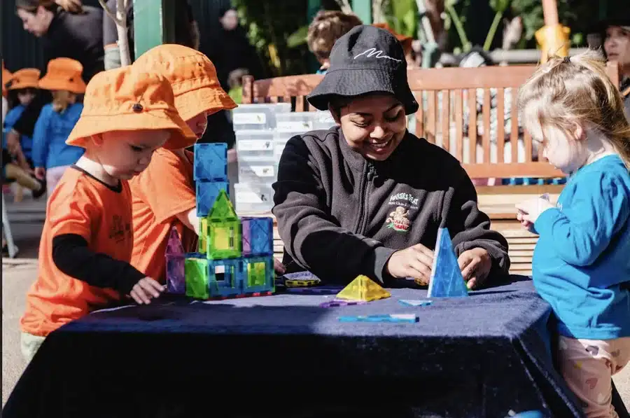 An educator and two children building with blocks at an outdoor table
